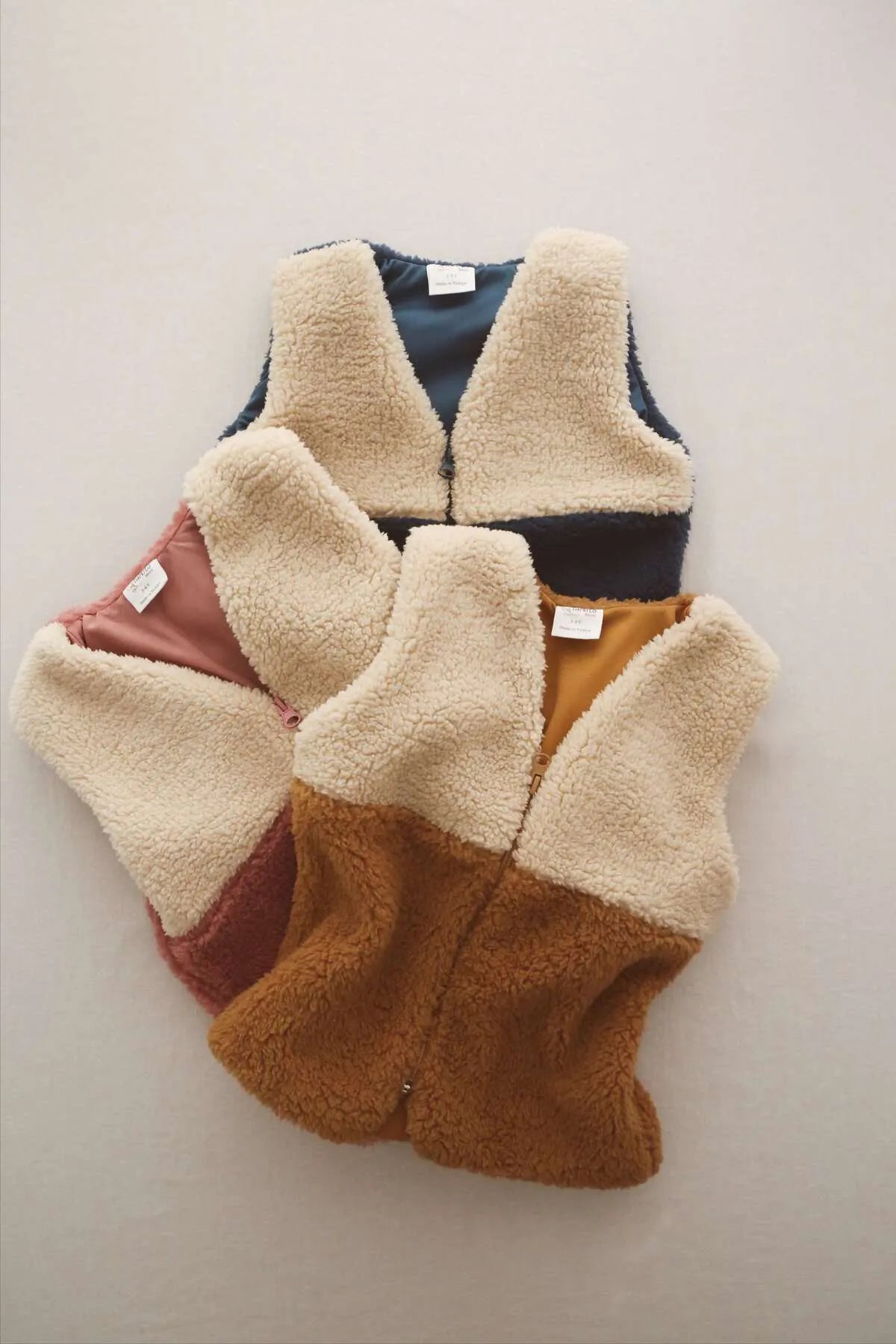 Cozy teddy vests in brown, navy, and pink, perfect for keeping babies warm and comfortable